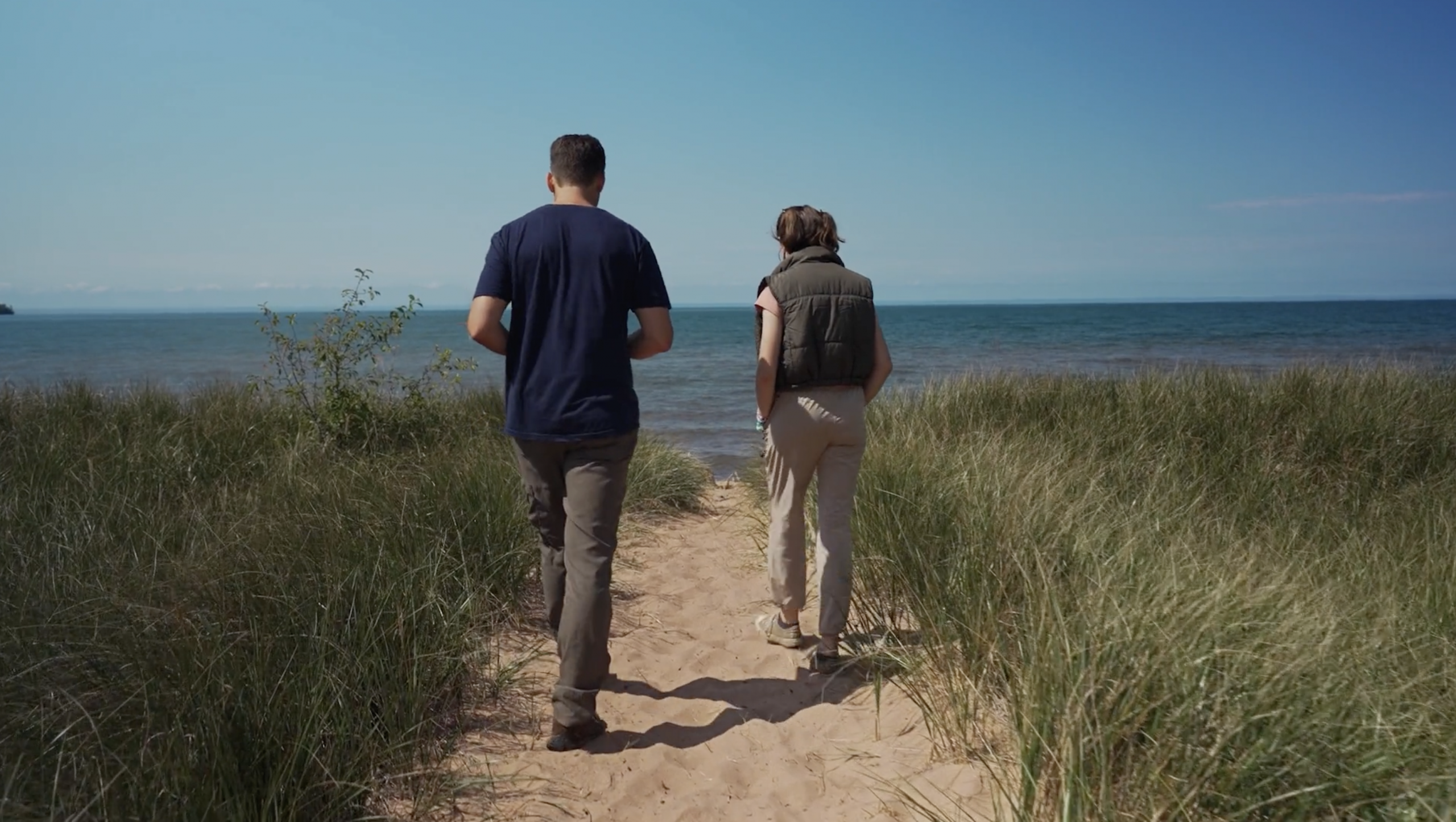 Mapping the Mysteries of the Great Lakes. Man and women walking on sand towards Great Lake
